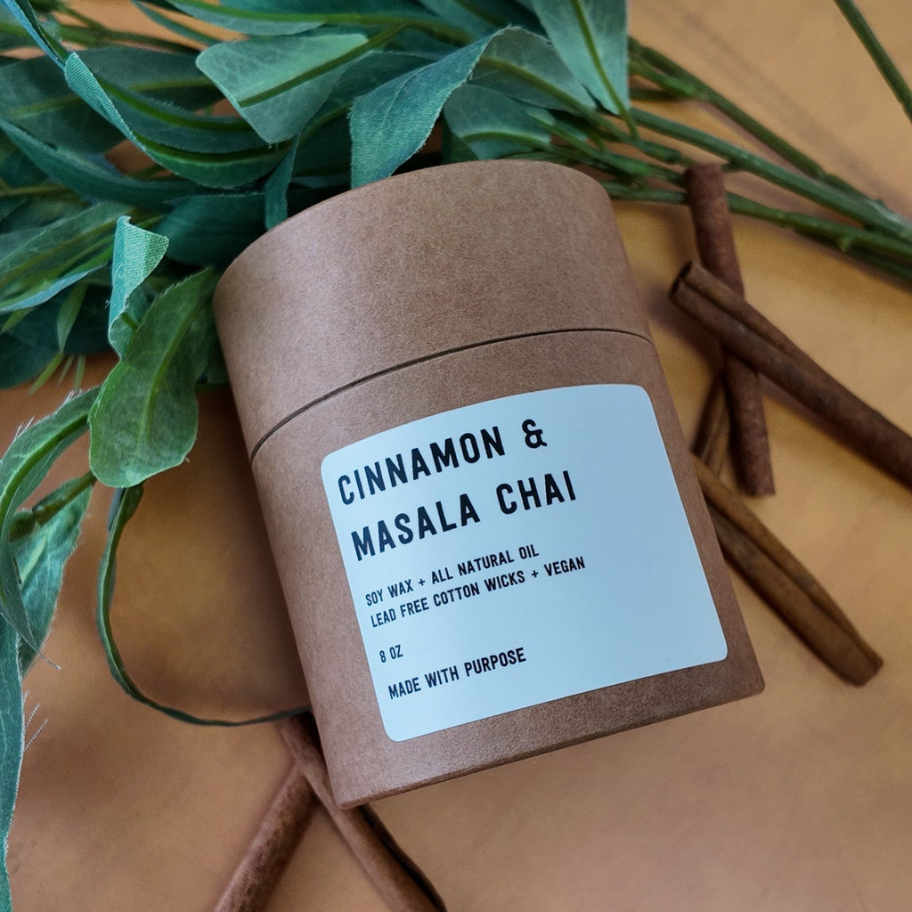 Candle labeled 'Cinnamon & Masala Chai' on a wooden surface with an orange background